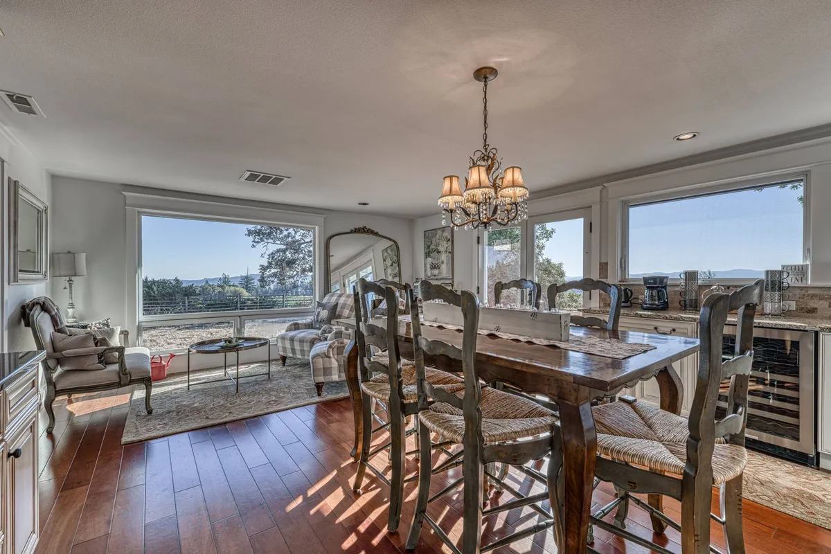 An elegant dining area with a large table beneath a chandelier, surrounded by windows that flood the space with light. A cozy seating area is visible nearby, creating a warm and welcoming environment for meals and gatherings.
