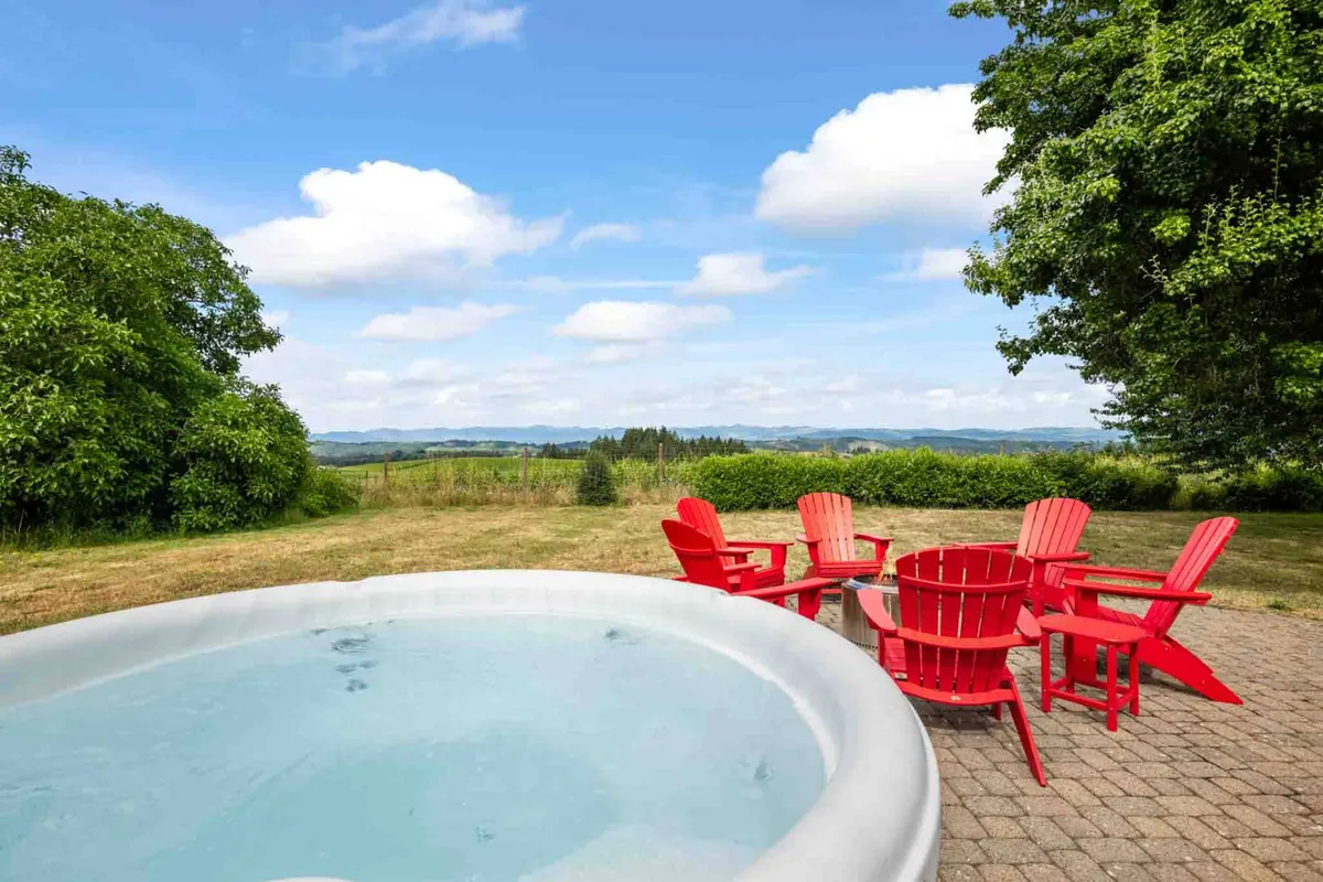 The image highlights a relaxing outdoor area with a hot tub, bright red chairs, and sweeping landscape views in the background. The scene is both inviting and connected to nature—perfect for unwinding after a day of exploration.