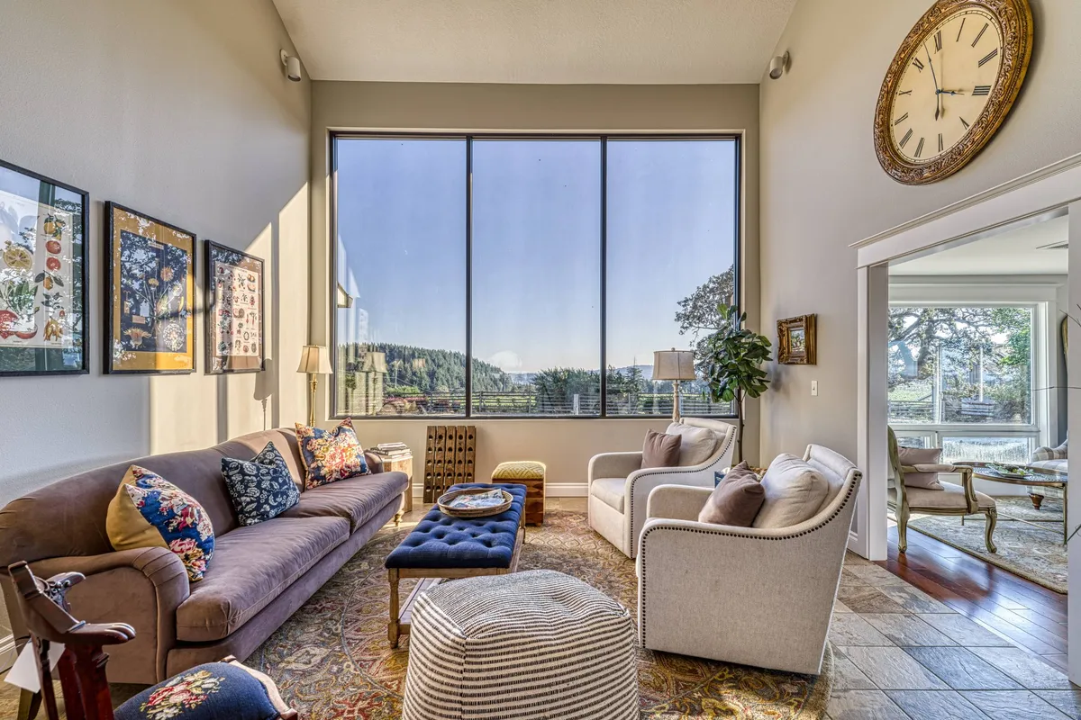 A comfortable seating area facing large windows that frame a scenic, tranquil view. The decor blends modern comfort with inviting touches such as decorative wall art and a clock, enhancing the relaxing atmosphere ideal for quiet moments or socializing.