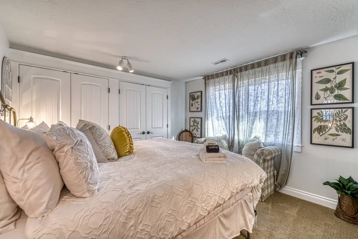 A tranquil master bedroom featuring a large bed dressed in plush, high-end linens. Sunlight filters softly through sheer curtains, illuminating botanical artwork on the walls and a cozy armchair by the window, evoking a serene sanctuary perfect for relaxation after a day of wine country exploration.