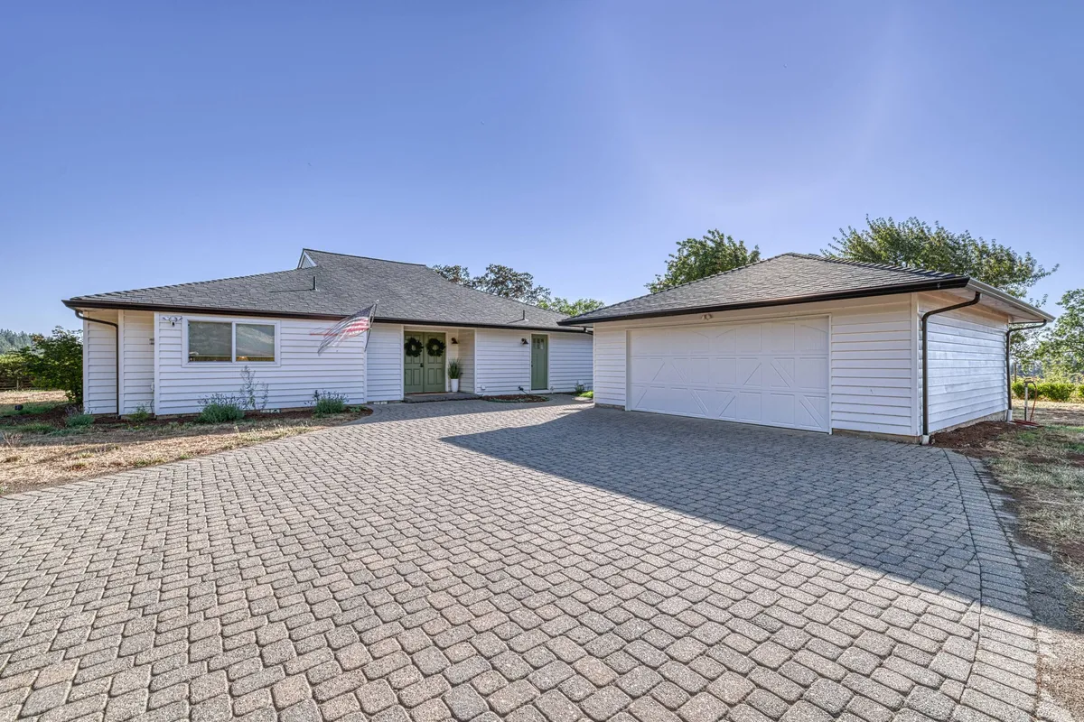 The elegant exterior of the property, showcasing the front door adorned with a wreath, a paved driveway, and a garage structure. The inviting entry hints at the upscale, private residence awaiting within.