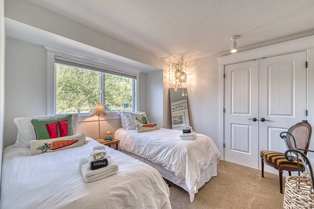 A guest bedroom outfitted with two twin beds, decorated with coordinated pillows and softly-lit by a lamp by the window. The flexible sleeping arrangement and cheerful accents make this an inviting space for couples or small families.