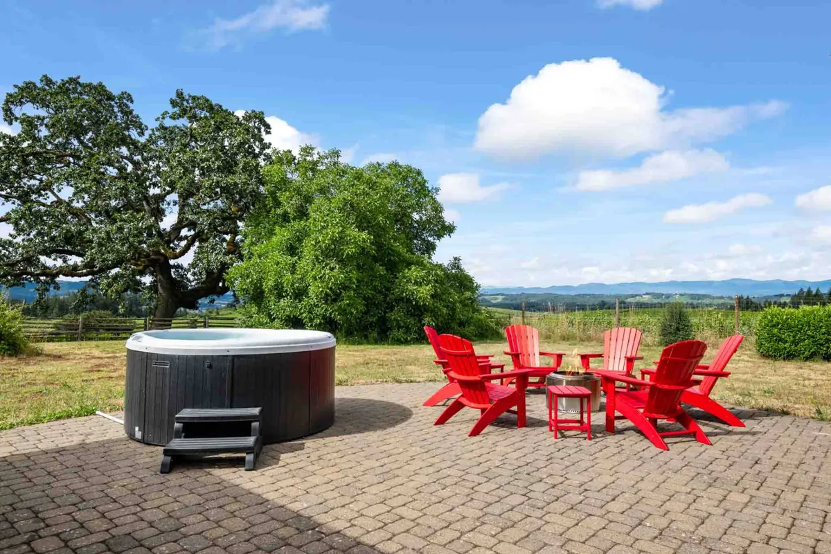 A welcoming outdoor patio featuring a bubbling hot tub, vibrant red chairs, and a lush green tree overlooking an open landscape—perfect for relaxation and socializing in a private setting.