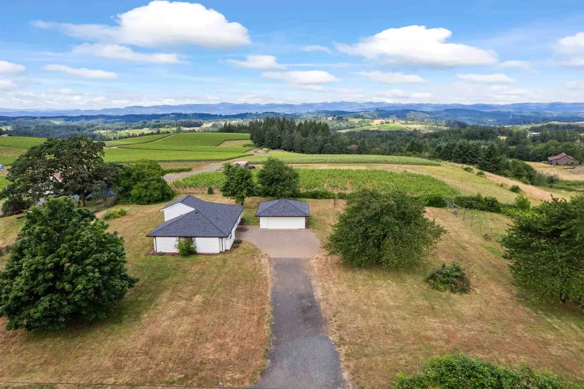 A sweeping exterior view of a stylish house set amid beautifully landscaped gardens, with rows of vineyards and a majestic mountain range in the distance. The scene evokes a sense of peaceful seclusion and idyllic wine country ambiance.